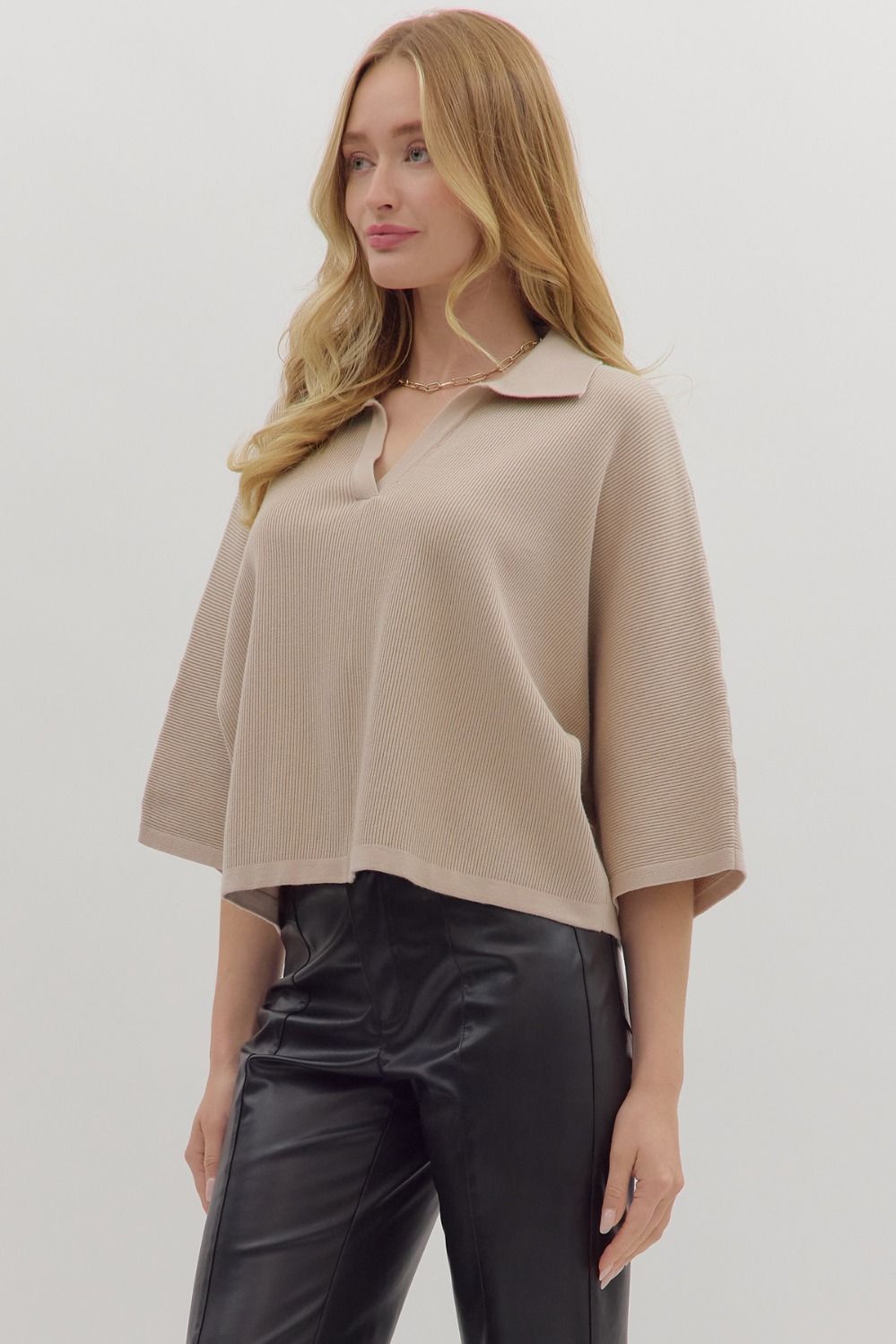 Woman wearing slightly cropped ribbed 3/4 sleeve beige knit sweater and black pants on a white background