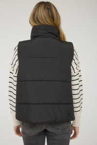 Back view of woman wearing a black puffer vest  over a striped sweater on a white background