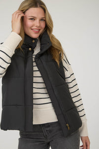 Woman wearing a black puffer vest with zipper closure over a striped sweater on a white background