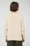 Back view of woman wearing a beige long sleeve round neck sweater against a plain background