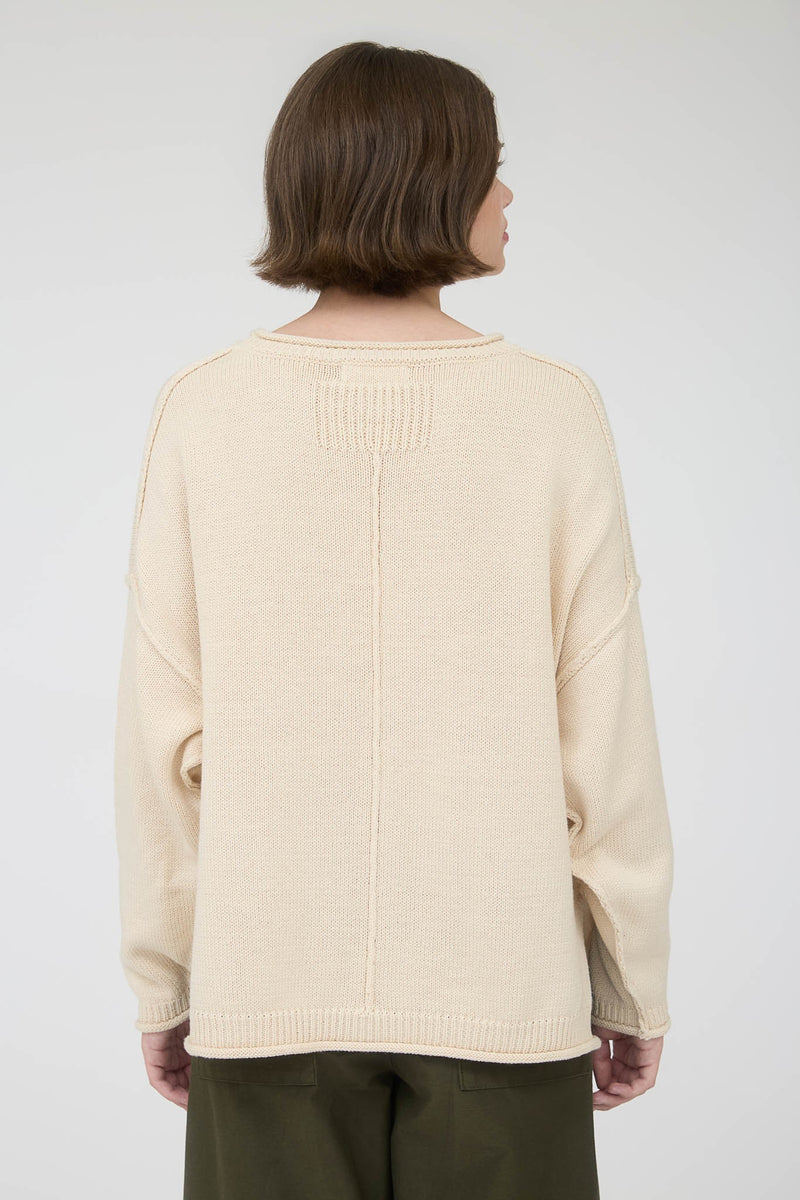 Back view of woman wearing a beige long sleeve round neck sweater against a plain background