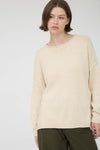 Woman wearing a beige long sleeve round neck sweater against a plain background