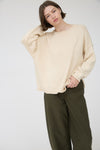 Woman wearing a beige long sleeve round neck sweater against a plain background