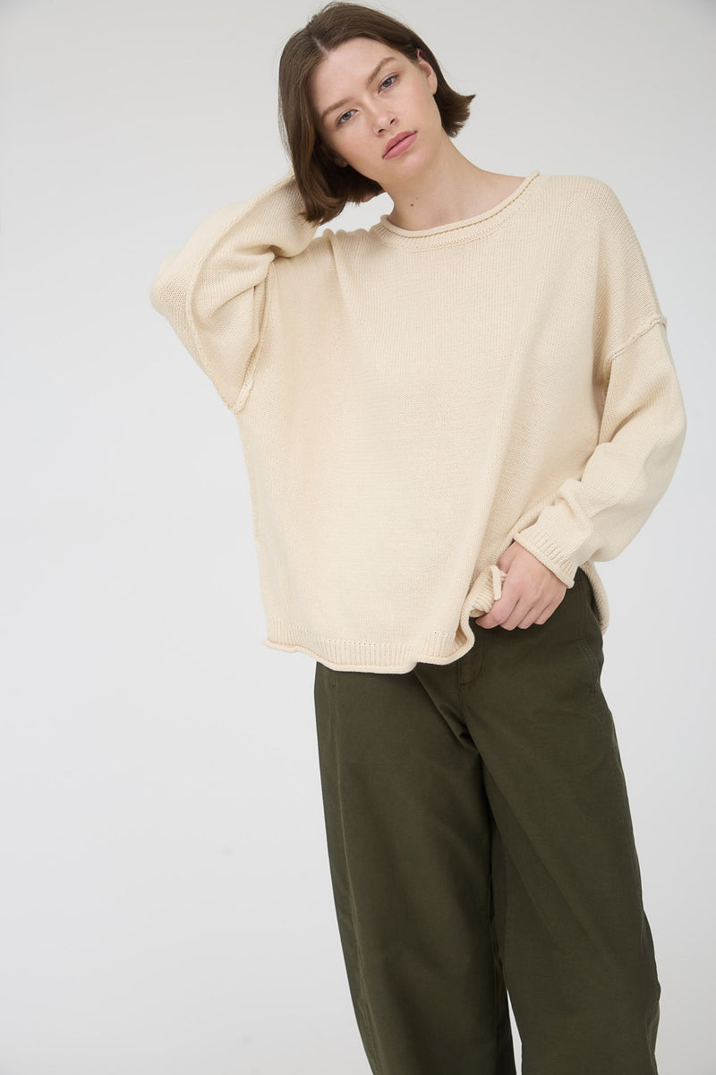 Woman wearing a beige long sleeve round neck sweater against a plain background