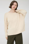 Woman wearing a beige long sleeve round neck sweater against a plain background
