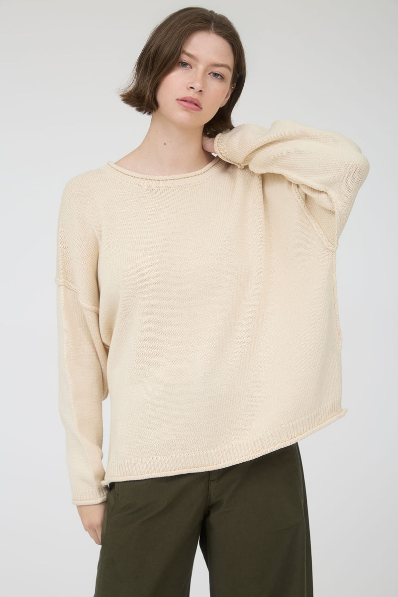 Woman wearing a beige long sleeve round neck sweater against a plain background
