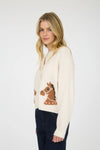 Woman profile view wearing a cream button front cardigan sweater with a horse head design on a white background