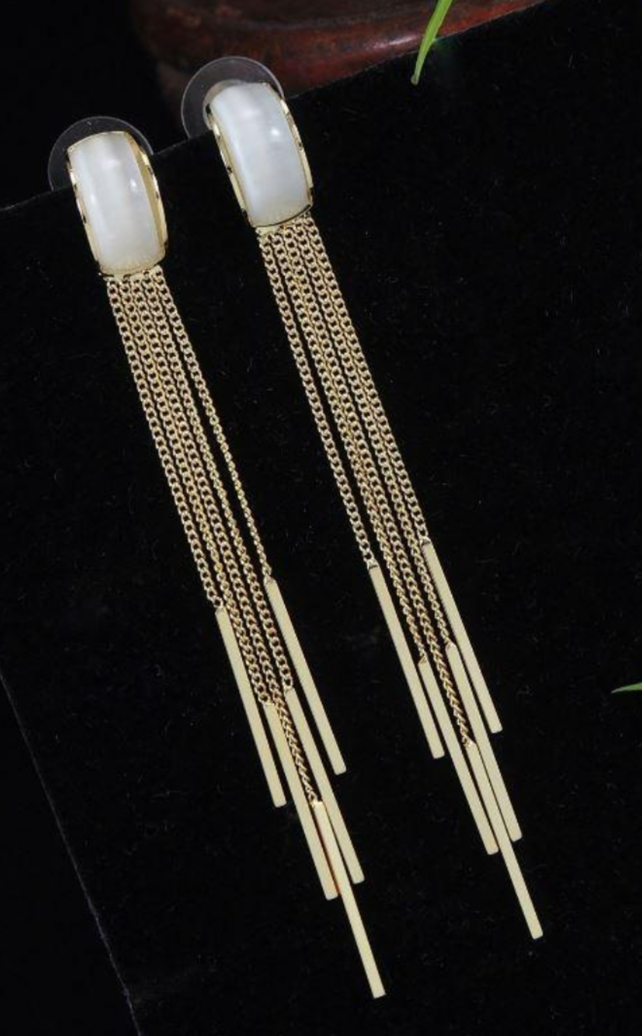 Gold earrings with long chains and white stones on a dark background