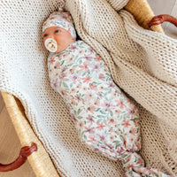 Newborn baby wrapped in a floral swaddle blanket with a pacifier, lying on a textured surface.