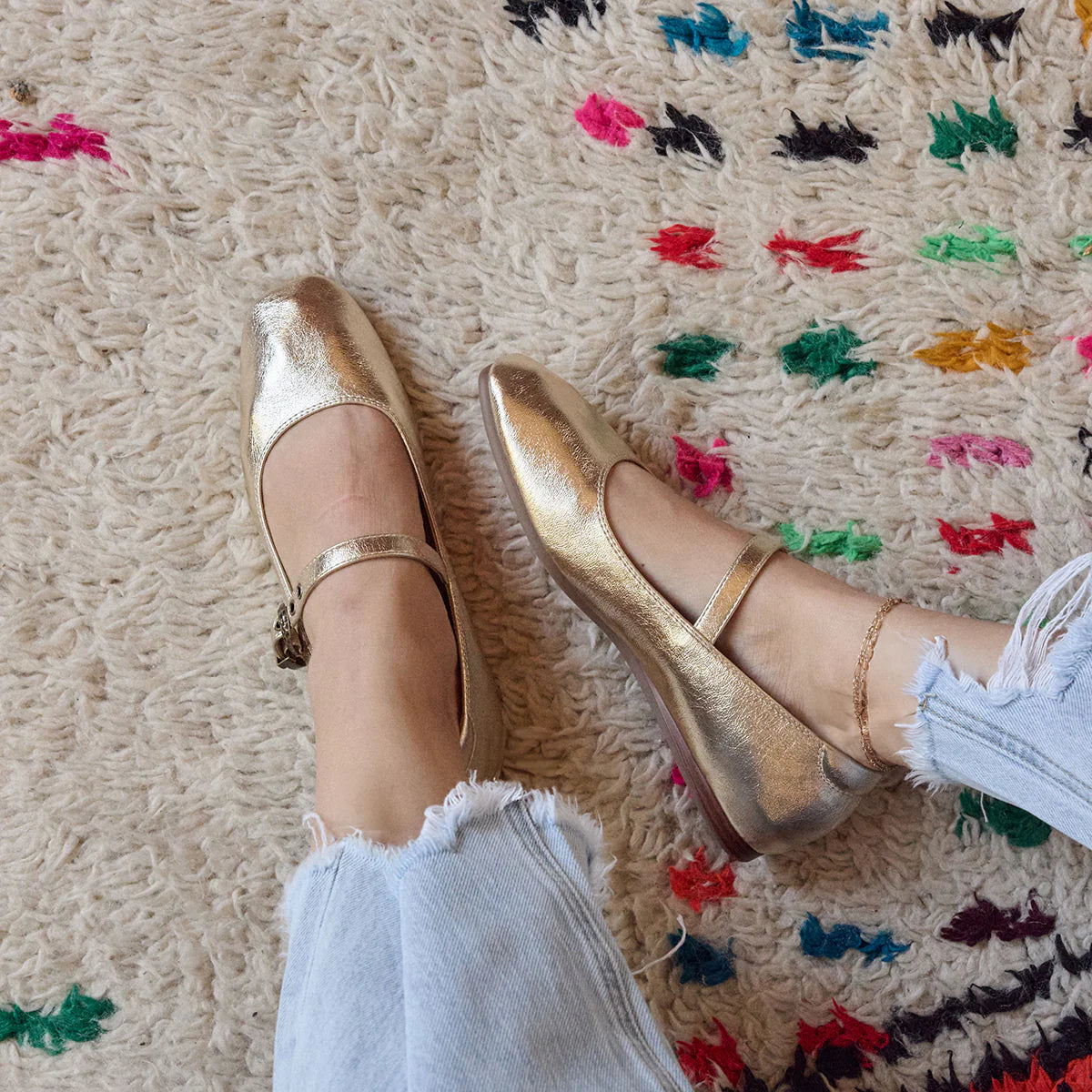 Gold metallic ballet flats with strap worn on a colorful rug