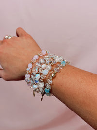 Close-up of a wrist wearing multiple beaded bracelets on a pink background