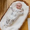 Baby in a horse and rider patterned onesie lying on a white blanket in a wooden crib.
