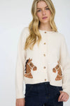 Woman wearing a cream cardigan with button front and horse head designs on a white background