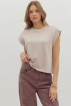 Woman wearing a beige sleeveless top and brown pants on a white background