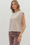 Woman wearing beige sleeveless top and brown pants on a white background
