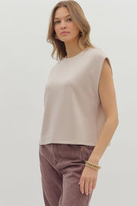 Woman wearing beige sleeveless top and brown pants on a white background