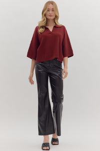 Woman wearing slightly cropped ribbed 3/4 sleeve burgundy knit sweater and black pants on a white background