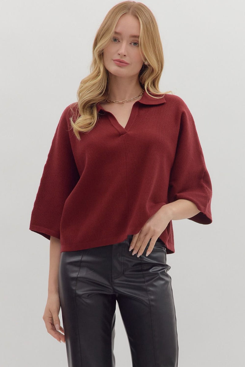Woman wearing slightly cropped ribbed 3/4 sleeve burgundy knit sweater and black pants on a white background