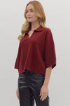 Woman wearing slightly cropped ribbed 3/4 sleeve burgundy knit sweater and black pants on a white background