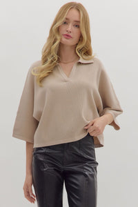 Woman wearing ribbed 3/4 sleeve beige knit sweater and black pants on a white background