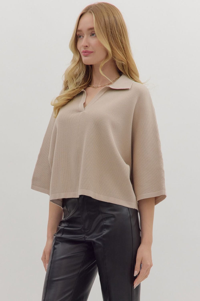 Woman wearing slightly cropped ribbed 3/4 sleeve beige knit sweater and black pants on a white background