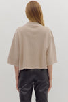 Back view of  woman wearing slightly cropped ribbed 3/4 sleeve beige knit sweater and black pants on a white background