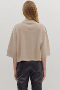 Back view of  woman wearing slightly cropped ribbed 3/4 sleeve beige knit sweater and black pants on a white background