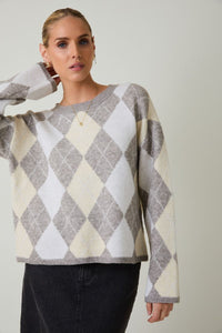 Woman wearing a round neck long sleeve gray and beige argyle sweater against a plain background