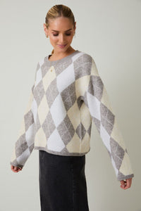 Side view of woman wearing a round neck long sleeve gray and beige argyle sweater against a plain background