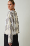 Back view of woman wearing a round neck long sleeve gray and beige argyle sweater against a plain background