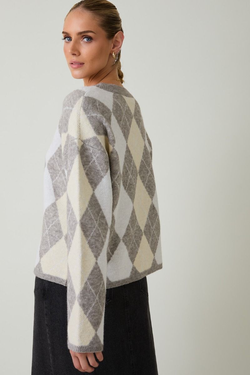 Back view of woman wearing a round neck long sleeve gray and beige argyle sweater against a plain background